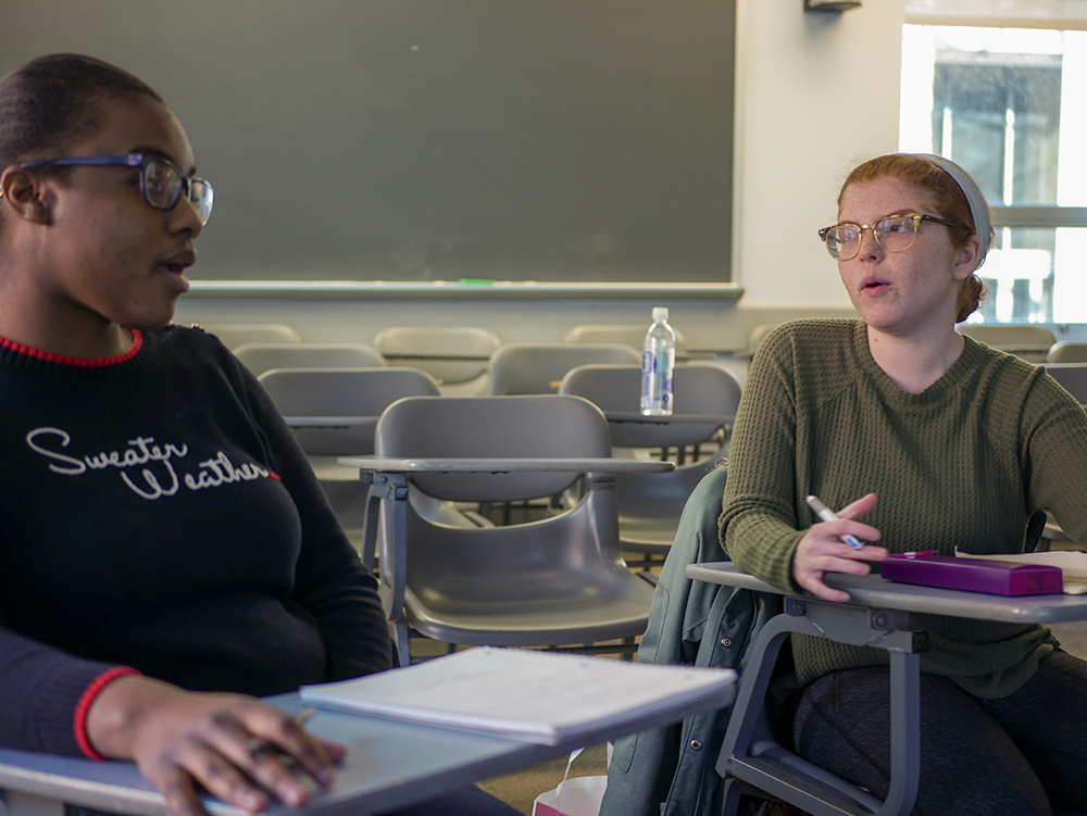 Two students stand with papers in their hands in discussion