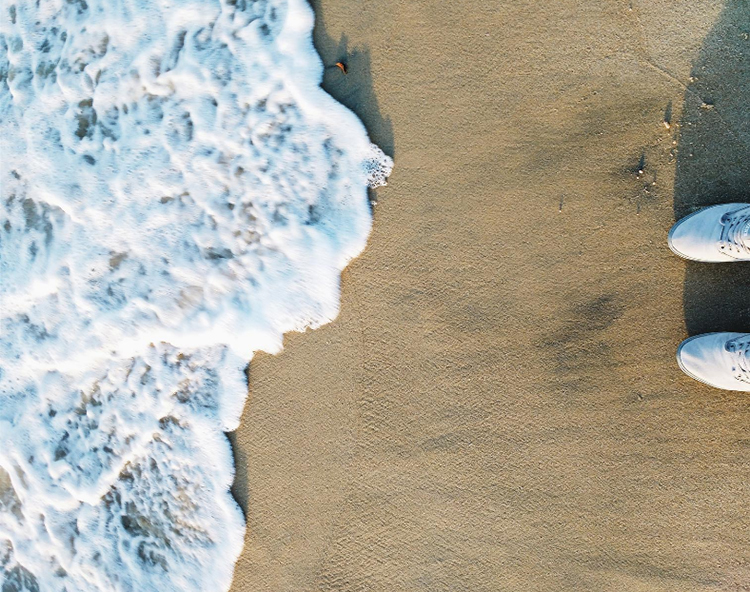 close up of white sneakers on the beach with water