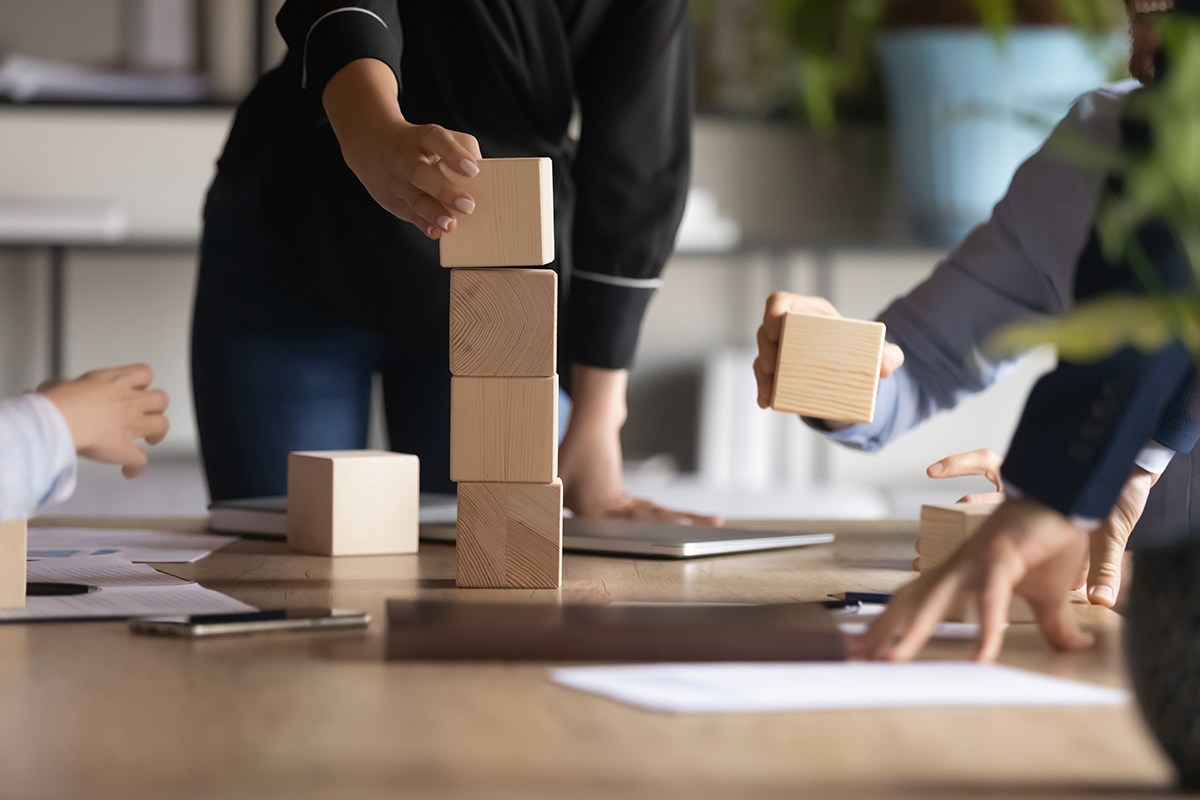 woman placing wooden building block on stack of other blocks