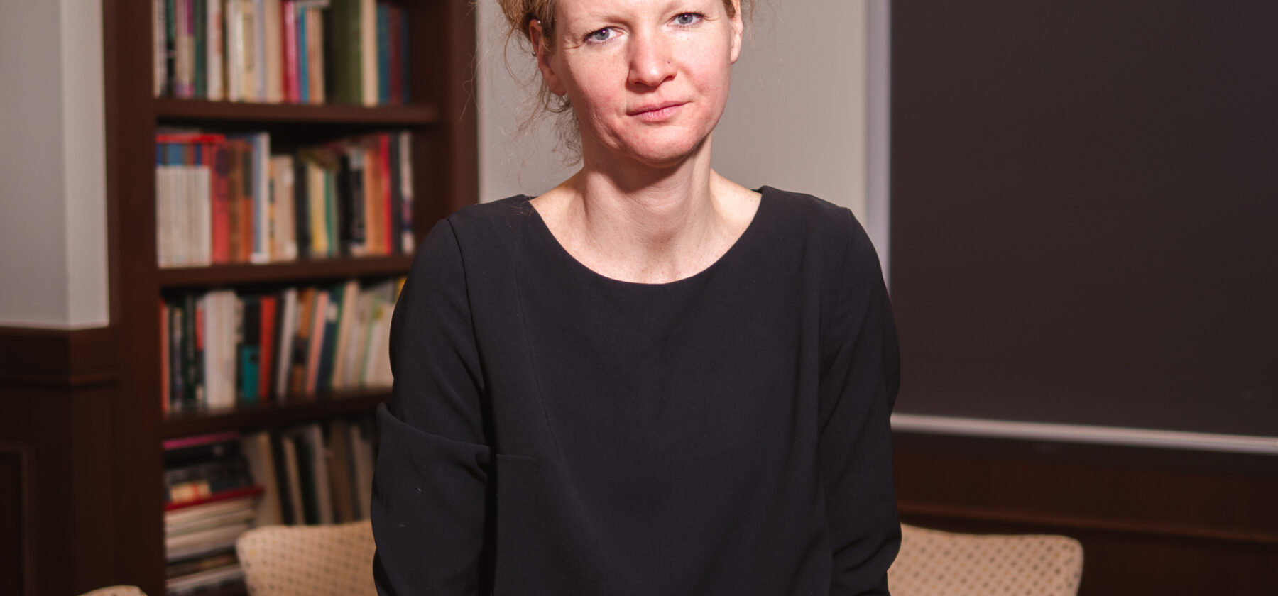 woman sitting on desk with bookshelf behind her