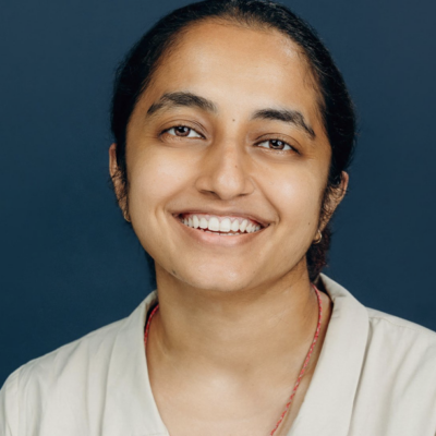 headshot of person with dark hair pulled back smiling at camera wearing tan top