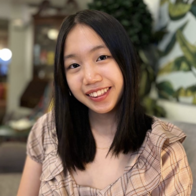 Headshot of woman with long black hair smiling at the camera wearing a brown and beige plaid top
