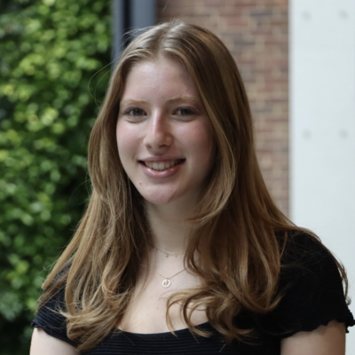 Headshot of woman with long light brown hair smiling at camera wearing black short-sleeved shirt