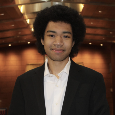 Headshot of man with black hair smiling at the camera wearing a black blazer and white shirt