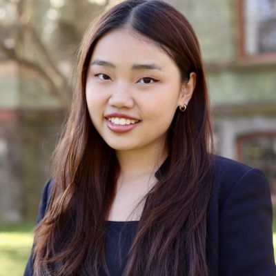 Woman with long auburn hair smiling at camera outdoors wearing a black blazer
