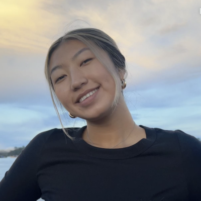 Woman with blonde hair pulled back smiling at camera outdoors with sunset in background wearing a black long-sleeved top