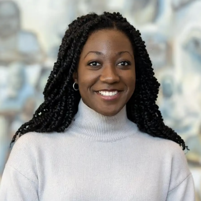 Female doctoral student with long black hair and dark skin smiling at camera wearing a white turtleneck sweater
