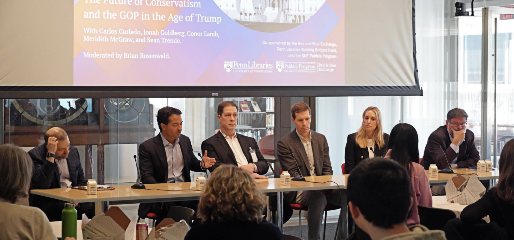 photo from panel discussion with six people seated at a long horizontal table with a screen behind them