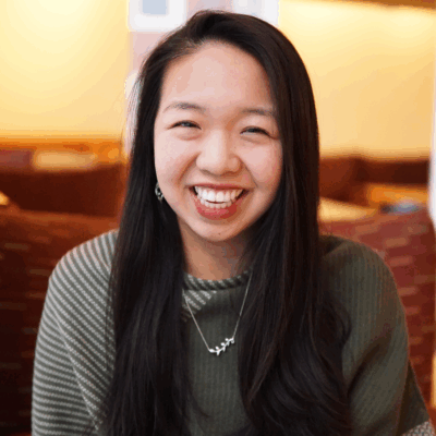 woman with light skin and long black hair wearing green sweater smiling for camera