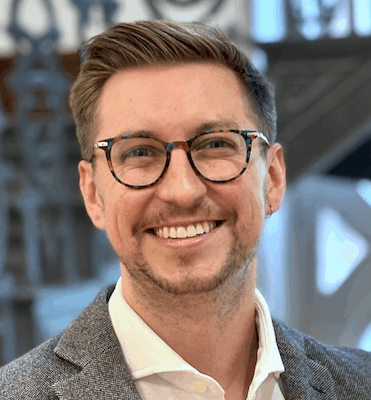 headshot for male graduate student with light skin and short light brown hair, wearing glasses and a wool blazer and white button down shirt