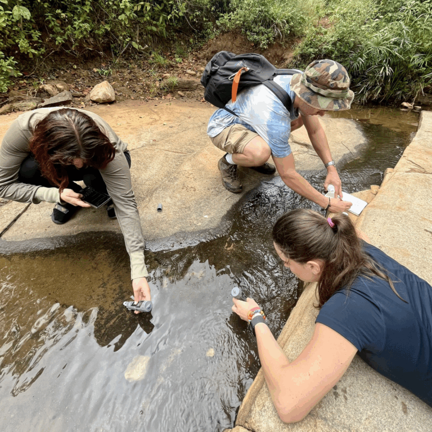 Photo of Griffin Pitt, with two other student researchers to test the conductivity, total dissolved solids, salinity, and temperature of water below a sand dam in Kenya.