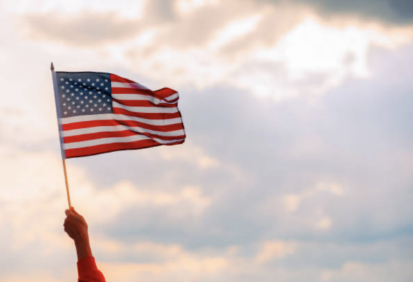 image of hand holding an American flag waving agains a cloudy sky