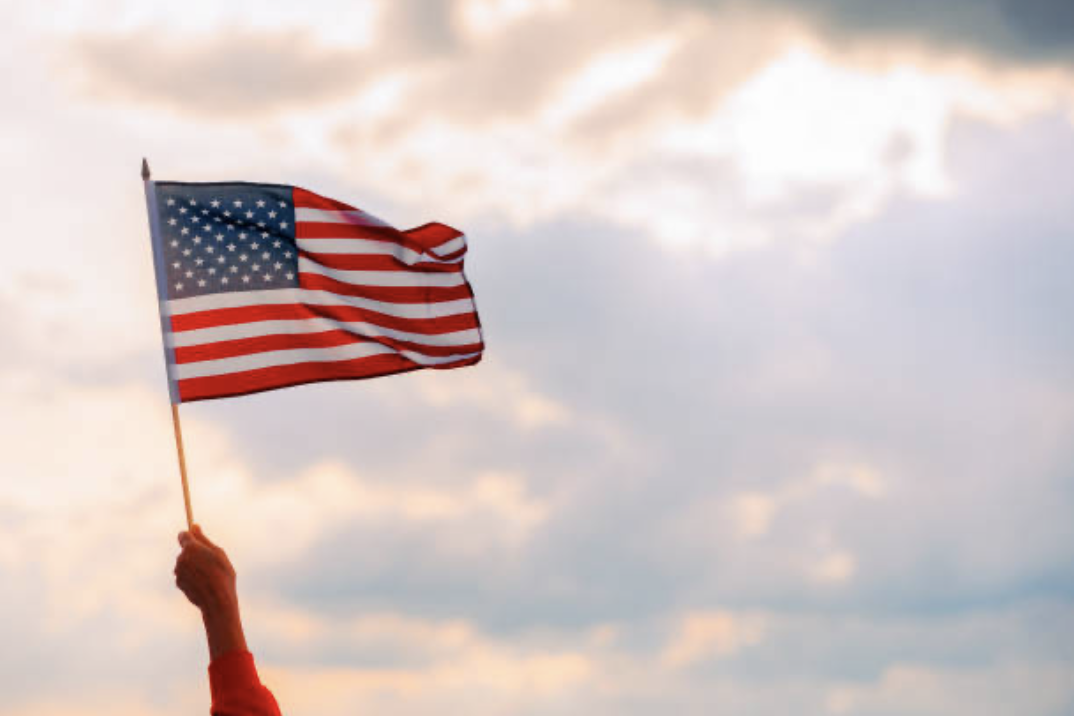 image of hand holding an American flag waving agains a cloudy sky